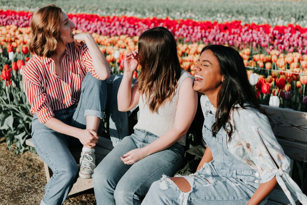 Three young women in healthy relationships sitting on a bench laughing. 